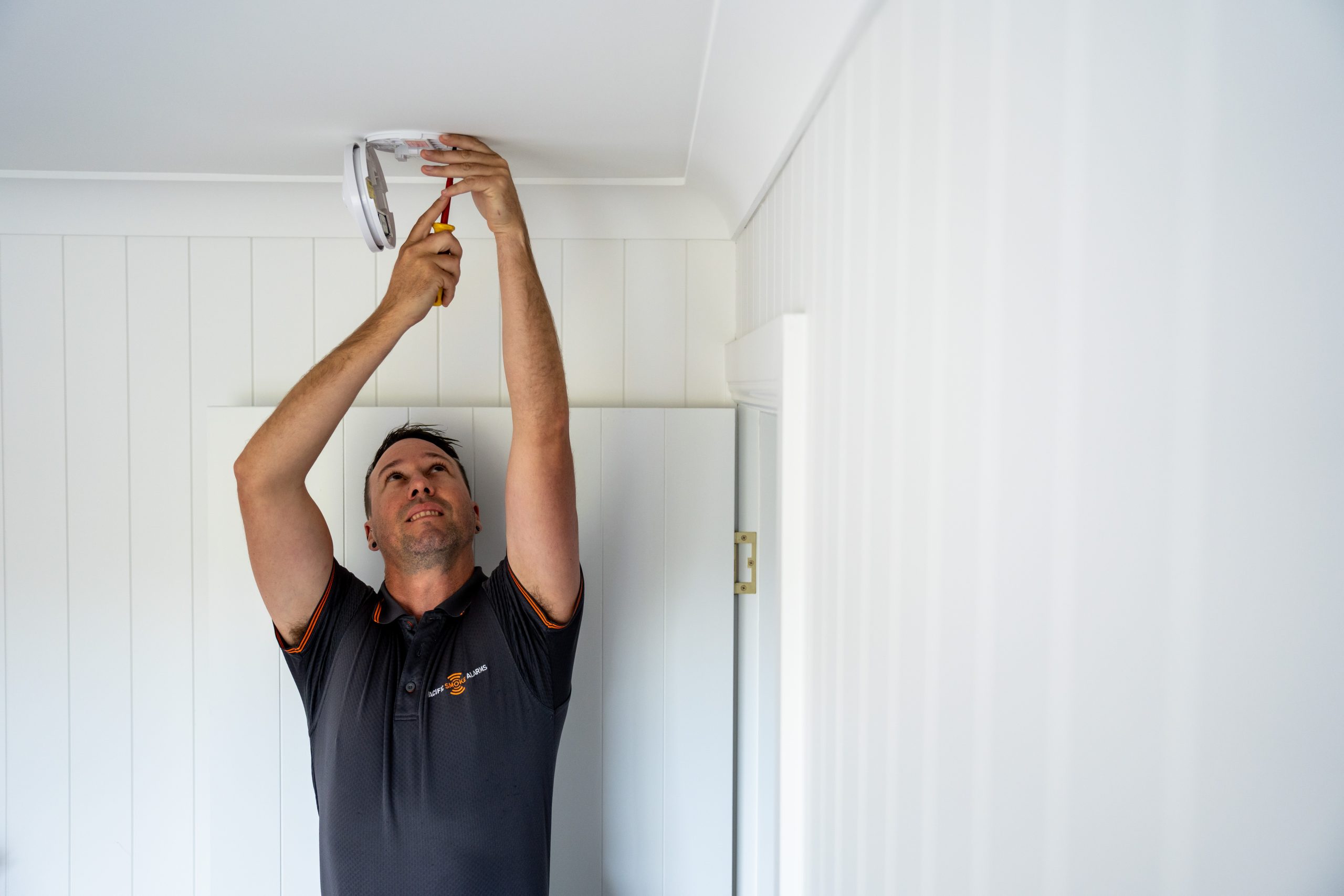 Licensed smoke alarm installer fitting an interconnected alarm in a Gold Coast home